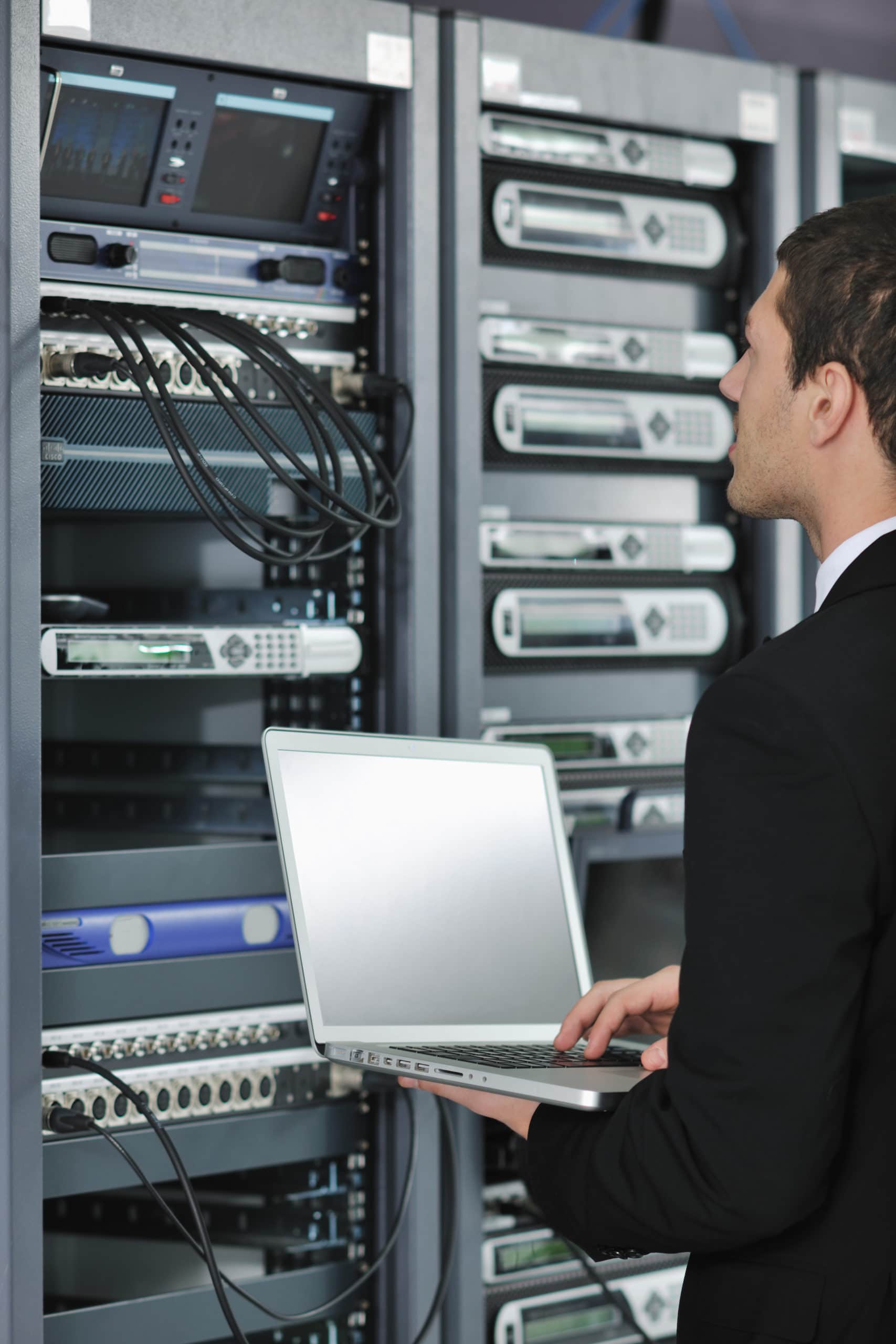 Businessman With Laptop In Network Server Room young engeneer business man with thin modern aluminium laptop in network server room