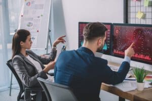 Two data analysts look at charts on computer screens while testing software.