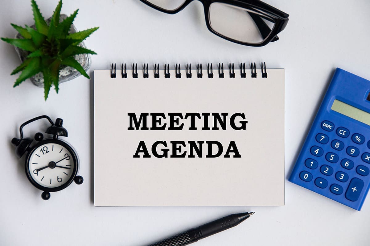 A notebook in the center of a table with the words “Meeting Agenda” on it.